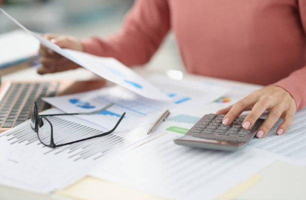 Business woman counting on calculator and holding documents in hands closeup. Bookkeeping concept